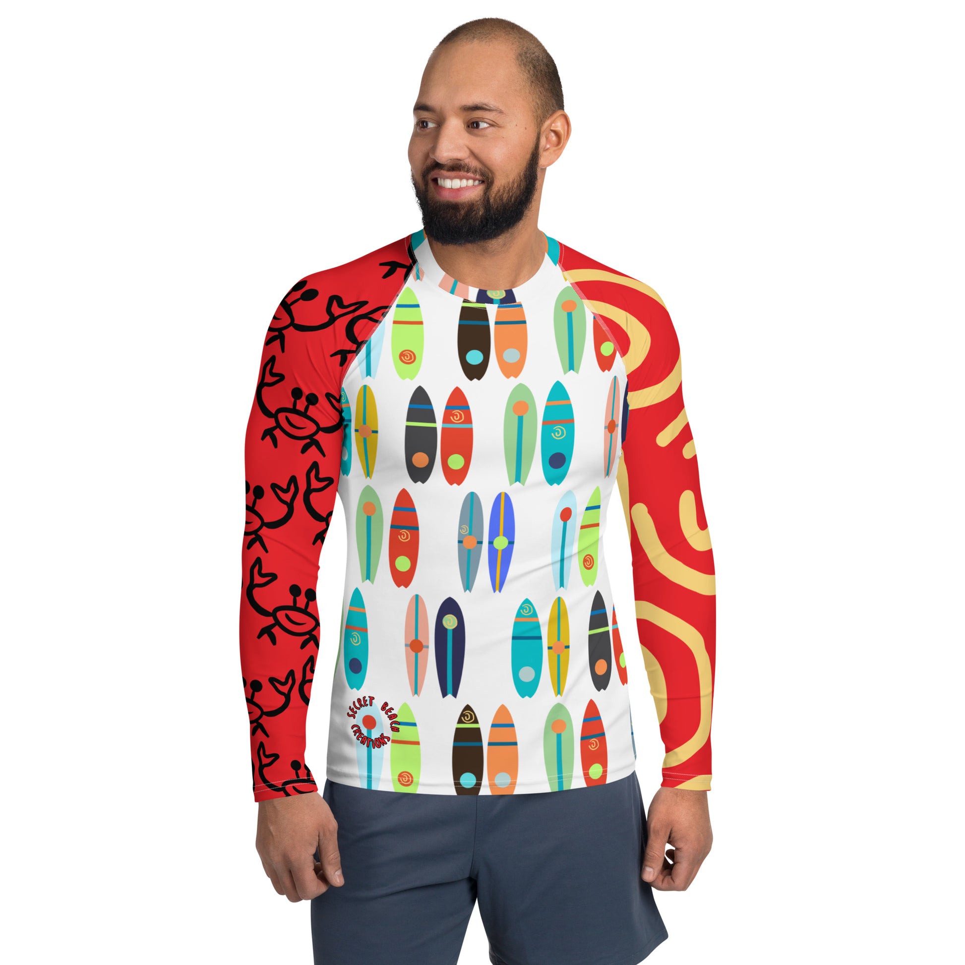 Image of a white long sleeve rash guard with red sleeves, yellow sun lines on one sleeve, outline of a happy ghost crab on the other, a pattern of paddle boards in the front with the words "Secret Beach Creations" on the lower left and a repeating paddle board pattern in the back.