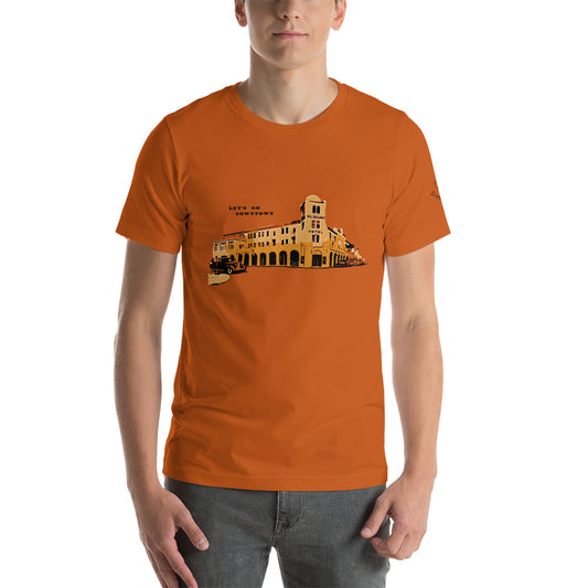 Image of a orange color t-shirt with a stylized building design with the words "Lets go downtown".